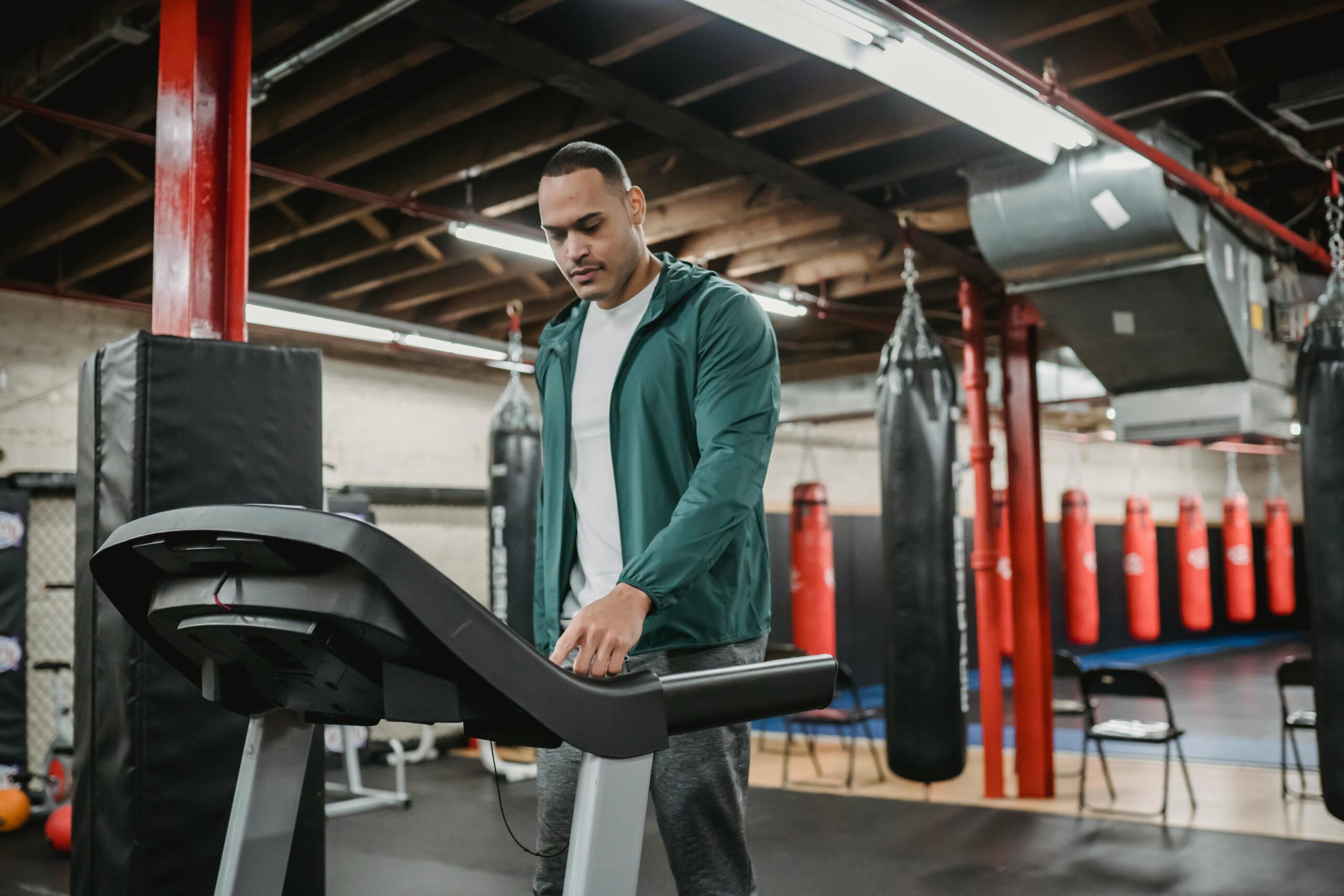 Serious sporty male in sportswear pressing buttons on treadmill while training in contemporary gym